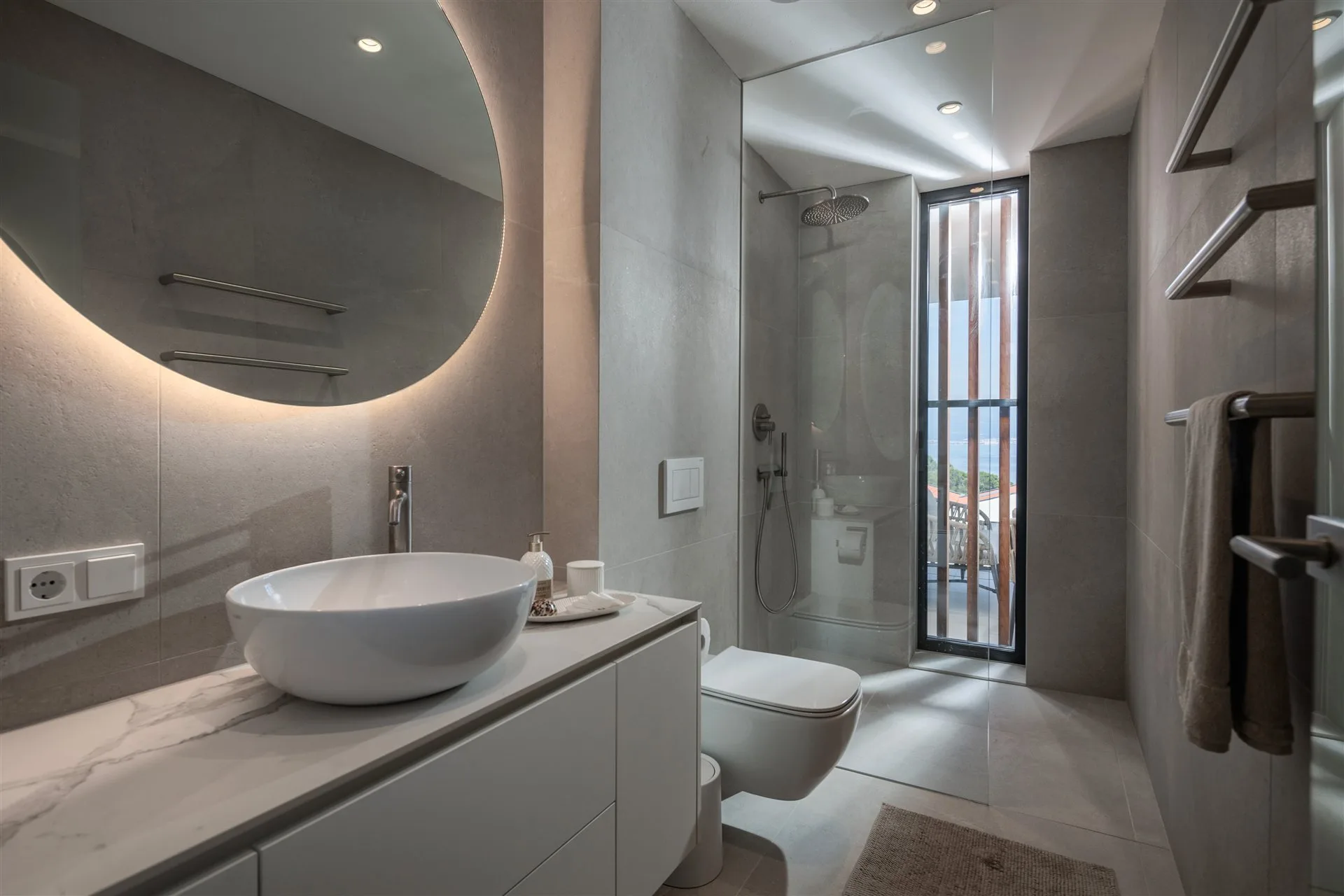 Villa Manatis en-suite Badezimmer mit rundem Spiegel und warmem Steinfinish